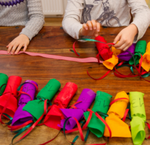 Zwei Kinder schnüren Adventsgeschenke in ein Band.