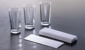 Drei Gläser stehen neben Blättern Papier.