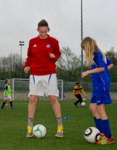 Die Trainerin Ronja übt mit einem Mädchen das Fußballspiel.