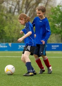 Ein Mädchen und ein Junge spielen gegeneinander Fußball.