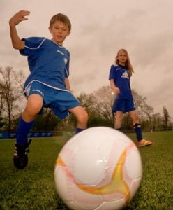 Ein Fußball ist auf uns zugerollt, ins Aus. Dahinter stehen zwei kindliche Fußballspieler.