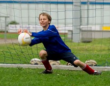 Ein Junge ist der Torwart. Er hält einen Ball.