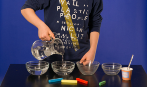 Ein Junge füllt Wasser in vier Glasschalen.