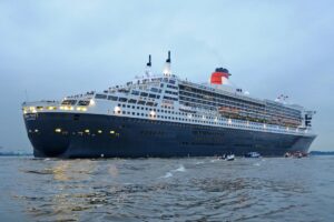 Das Kreuzfahrtschiff Queen Mary fährt am Abend mit Lichtern an Bord.