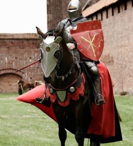 Ein Ritter sitzt in einem Burghof in einer Ritterrüstung auf einem Pferd.