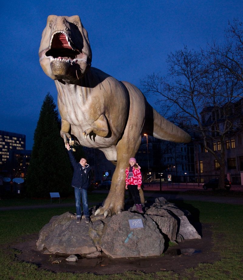 Zwei Kinder stehen vor einem großen Modell eines Tyrannosaurus Rex.