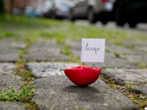 Ein kleines Boot aus Knete steht auf einem Straßenboden. Daran ist eine Fahne befestigt.