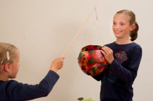 Ein Mädchen hält eine Ballonlaterne mit einem Stock hoch. Ein anderes Mädchen umschließt die Laterne mit ihren Händen.