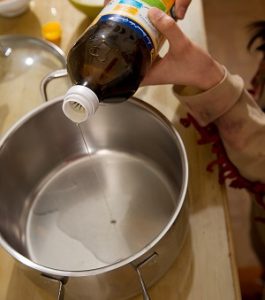 Aus einer Flasche kommt Öl in einen Topf.