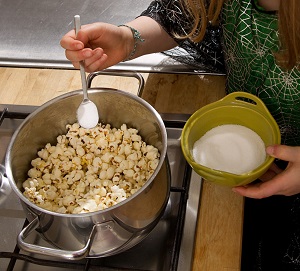 Der Junge streut Zucker auf das Popcorn.