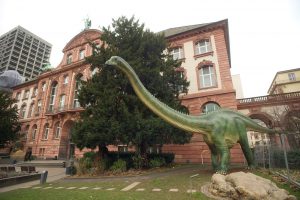 Das Senckenberg Museum in Nürnberg. Vor ihm steht ein großes Modell eines Dinosauriers.