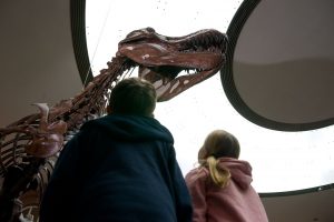 Zwei Kinder stehen unter einem Knochen-Gerüst eines Dinosauriers.