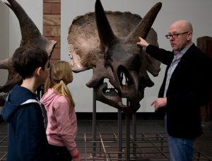 Dr. Herkner zeigt zwei Kindern den Knochen eines Triceratops.