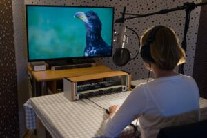 Eine Frau sitzt vor einem Bildschirm. Sie ist die Sprecherin Nele. Der Bildschirm zeigt einen Adler.