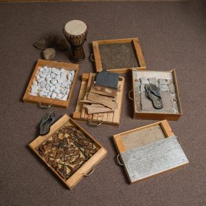 Es stehen mehrere Geräte um Geräusche zu erzeugen auf dem Boden. Das sind. Steine, Laub, Sand, Holz, Erde und eine Trommel.