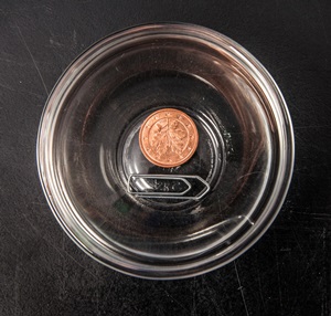 Eine Büroklammer und eine 1-Cent-Münze liegen in einer Schale aus Glas.
