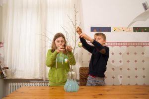 Zwei Kinder behängen Zweige mit bemalten Eiern.