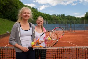 Zwei Mädchen stehen mit Tennisschlägern auf einem Tennis-Platz. Sie heißen beide Rebecca und sind 16 und 17. Jahre alt.