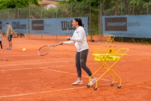 Eine Frau spielt einen Ball mit einem Tennisschläger. Sie heißt Lana und ist eine Trainerin.