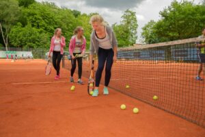 Die Mädchen Rebecca, Rebecca und Victoria sammeln Bälle auf einem Tennisfeld ein.