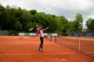 Das Mädchen Rebecca spielt mit ihrem Tennisschläger einen hohen Ball über das Netz.