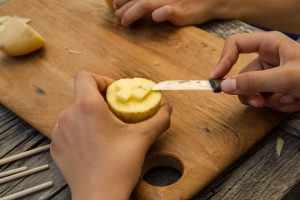 Ein Mädchen schneidet eine Kartoffel so, dass die gezeichnete Form hervorsteht.