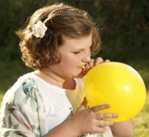 Ein Mädchen bläst einen gelben Luftballon auf.