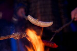 Kinder halten Würstchen und Stockbrot in das Lagerfeuer. 