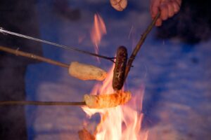 Mehrere Stöcke halten Würste und Stöcke in ein Feuer.