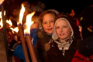 Einige Kinder halten Fackeln. Sie tragen Winterkleidung. 