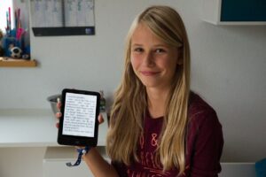 Das Mädchen Charlotte hält einen E-Reader hoch. 