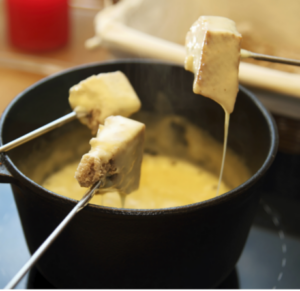 Drei Gabeln halten Brotstücke in einen Fonduetopf mit Käse.