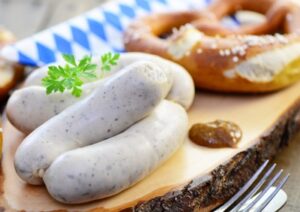 Eine Brezel und Weißwürste liegen neben Senf auf einem Brett.