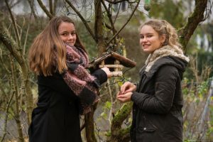Lotte und Marit stehen in einem Wald. Sie sind zwei 14.-jährige Mädchen. Lotte zeigt auf ein Vogelhaus.