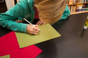 Ein Junge malt Tannenbäume auf ein goldenes Papier.
