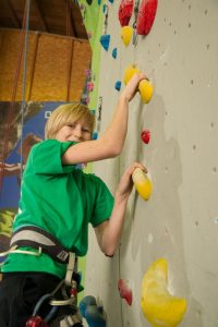 Das Mädchen Manina zeigt die Griffe an einer Kletterwand.