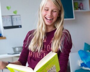 Das Mädchen Charlotte liest einen Comic. Sie lacht laut auf.