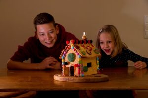 Zwei Kinder schauen auf ein Lebkuchenhaus auf einem Tisch.