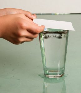 Eine Hand legt ein Stück Papier auf ein Glas mit Wasser.