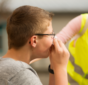 Ein Junge hält sich die blutende Nase mit einem Taschentuch zu.