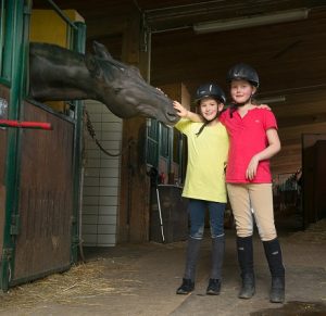 Die Mädchen Marlene und Janne stehen mit Reithelmen in einem Pferdestall.