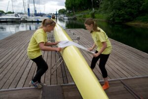 Zwei Mädchen putzen ein Ruderboot.