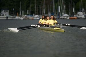 Ein Ruderboot mit vier Kindern von vorne. Sie haben alle zwei Ruder.