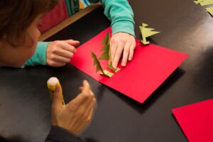 Ein Junge klebt goldene Tannenbäume auf ein rotes Papier.