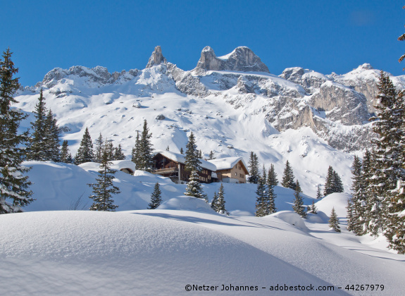 Verschneite Berggipfel in den Alpen. Eine Almhütte steht unter den Gipfeln.