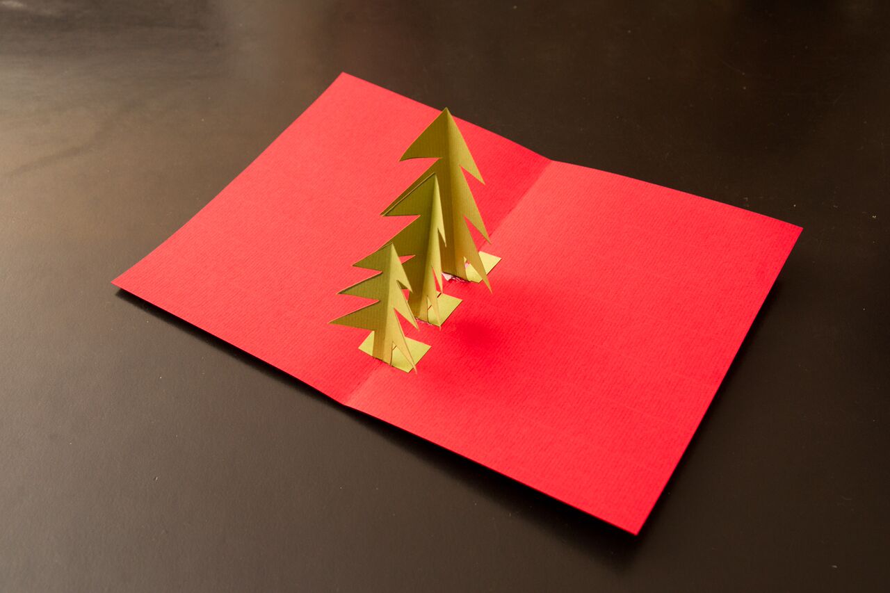 Auf einem roten Papier sind drei goldene Weihnachtsbäume gebastelt.
