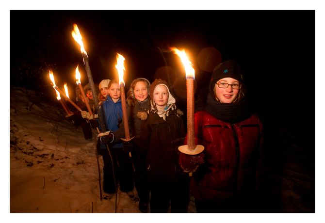 Sechs Kinder stehen hintereinander. Es ist Nacht. Die Kinder tragen alle Fackeln.