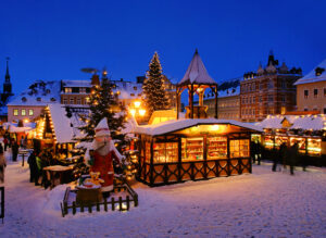 Ein nächtlicher Weihnachtsmarkt in einer Innenstadt. Die Stände und Wege sind voller Schnee.