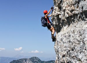 Ein Mensch klettert eine Steinwand in den Alpen hoch. Er trägt Schutzkleidung.