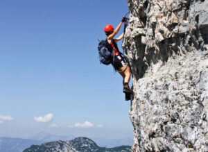 Ein Mensch klettert eine Steinwand in den Alpen hoch. Er trägt Schutzkleidung.